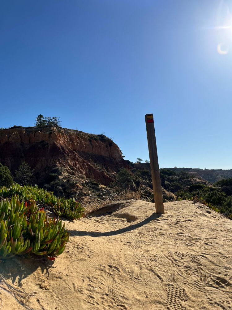 Sandy southern Portugal hiking path with trail marker and bright sun.