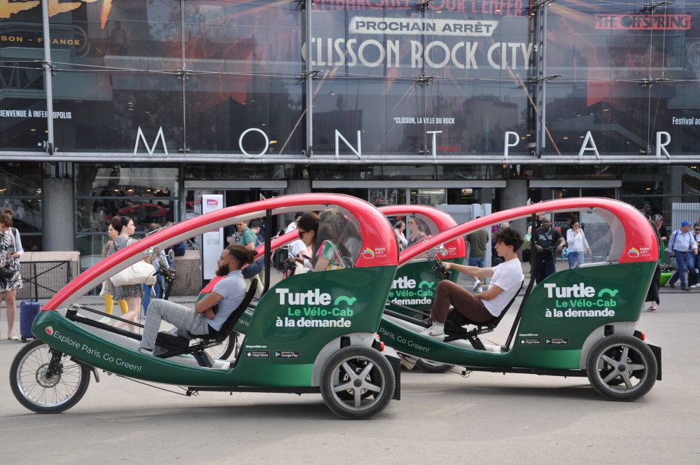 3 Turtle pedicabs at the train station with clients inside.